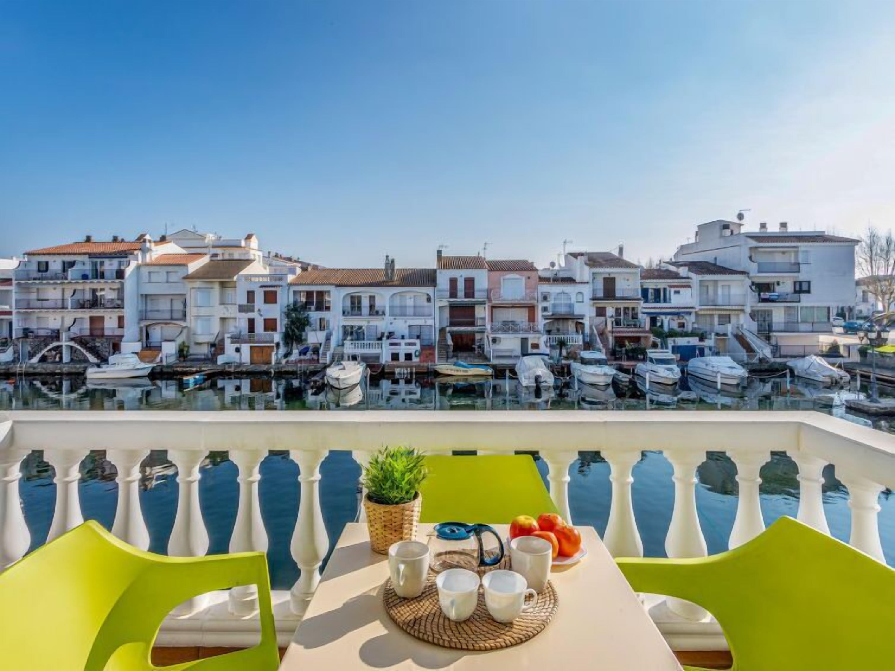 Una terraza con una mesa preparada para dos, con vista a un puerto deportivo con barcos y edificios al fondo.