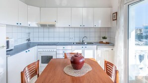 A modern kitchen with white cabinets, a wooden dining table, and a view through a large window. - Port Banyuls by Interhome (Empuriabrava)