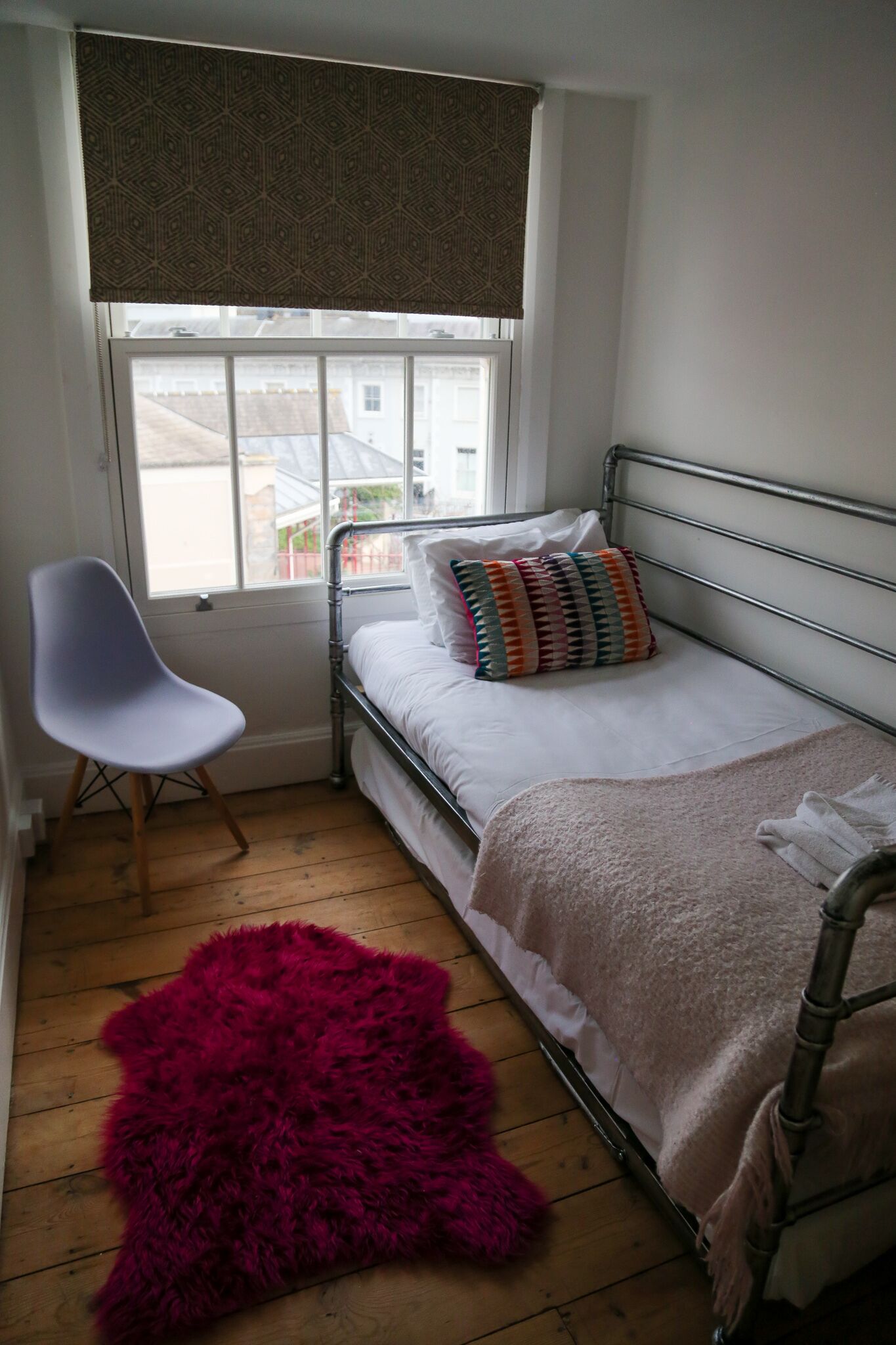 A small, tidy room with a single bed, a chair, and a large window.