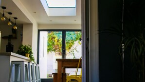 A modern interior with a skylight, a dining area with a wooden table and yellow chairs, and a kitchen with stools and plants. - Luxury 4BDR cottage right in the heart of Brighton (Brighton)