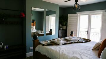 A bedroom with a large bed, a ceiling fan, a mirror, and a window with white shutters.