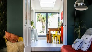 A room with a wooden floor, a red sofa, a white furry chair, and a dining area with yellow chairs and a wooden table. - Luxury 4BDR cottage right in the heart of Brighton (Brighton)