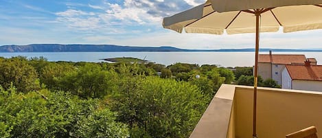 Un balcón con vista a un lago y montañas distantes, una sombrilla y una silla.