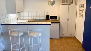 A compact kitchen with white cabinets, a microwave, a coffee maker, and a small island with stools.