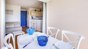 A dining area with a table set for two, a blue basket, and a kitchen in the background.