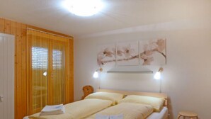 Una cama doble con dos almohadas y una mesita de noche, una puerta de madera y una ventana con persianas.