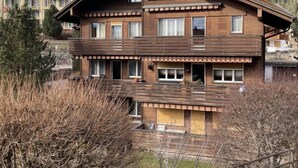 Un edificio de madera de varios pisos con balcones, rodeado de árboles y con montañas al fondo.