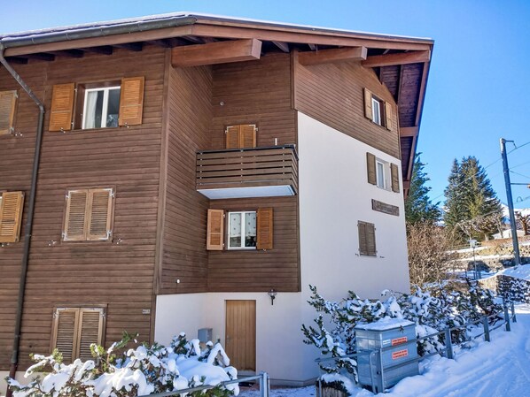 A multi-story wooden building with balconies and windows, surrounded by snow-covered trees and a clear sky.