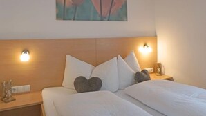 A hotel room with a wooden headboard, two bedside lamps, and a painting of flowers on the wall. - Schaller by Interhome (See)