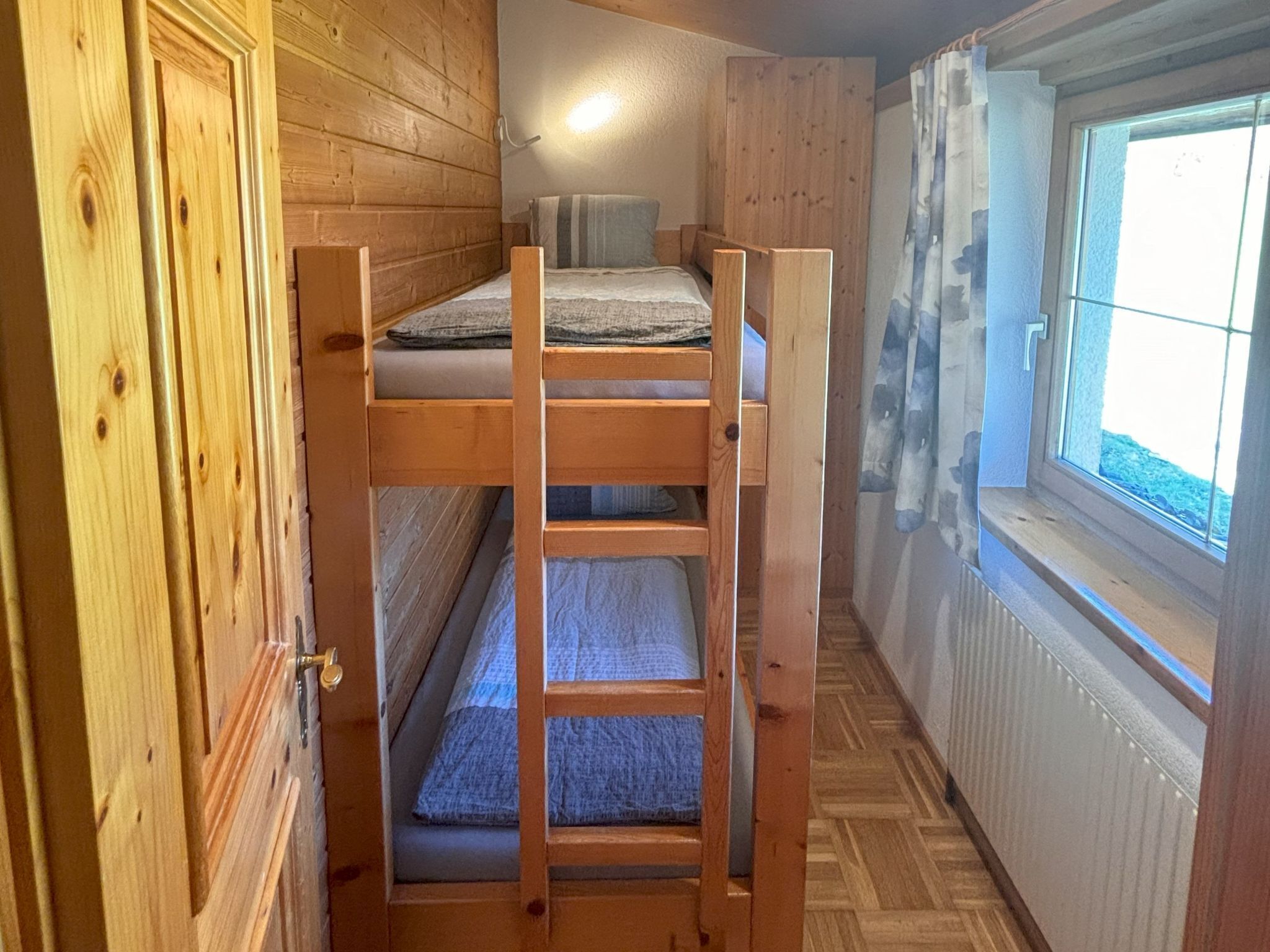 A bunk bed in a room with wooden walls and a window.