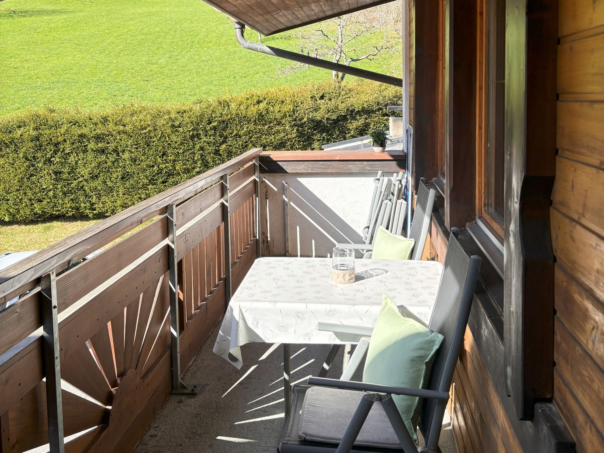 Un balcon avec une table et des chaises, une vue sur une pelouse verdoyante et une clôture en bois.
