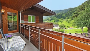Ein Holzbalkon mit Blick auf ein grünes Tal und Hügel.