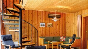 Ein gemütliches Zimmer mit einer Wendeltreppe, Holzwänden, einem grünen Sofa und einem Esstisch, der mit Tellern, Gläsern und Speisen gedeckt ist.