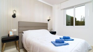 A bedroom with a large bed, a nightstand, a wall-mounted lamp, and a window with a view of greenery. - Apartment Pinazo by Interhome (Moraira)