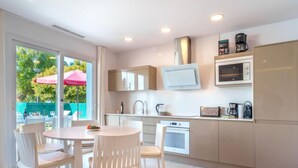 Una cocina moderna con armarios blancos, microondas, cafetera y un comedor con sillas y mesa blancos.