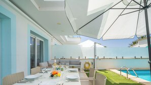 Zona pranzo con tavolo apparecchiato per quattro persone, posti a sedere all'aperto, piscina e patio coperto.