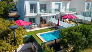 Una casa moderna de dos pisos con piscina, mobiliario de exterior y un balcón.