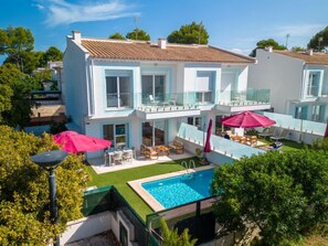 Ein modernes, zweistöckiges Haus mit Swimmingpool, Sitzgelegenheit im Freien und einem Balkon.