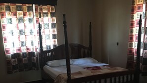 A bedroom with a four-poster bed, a black rug, and patterned curtains.