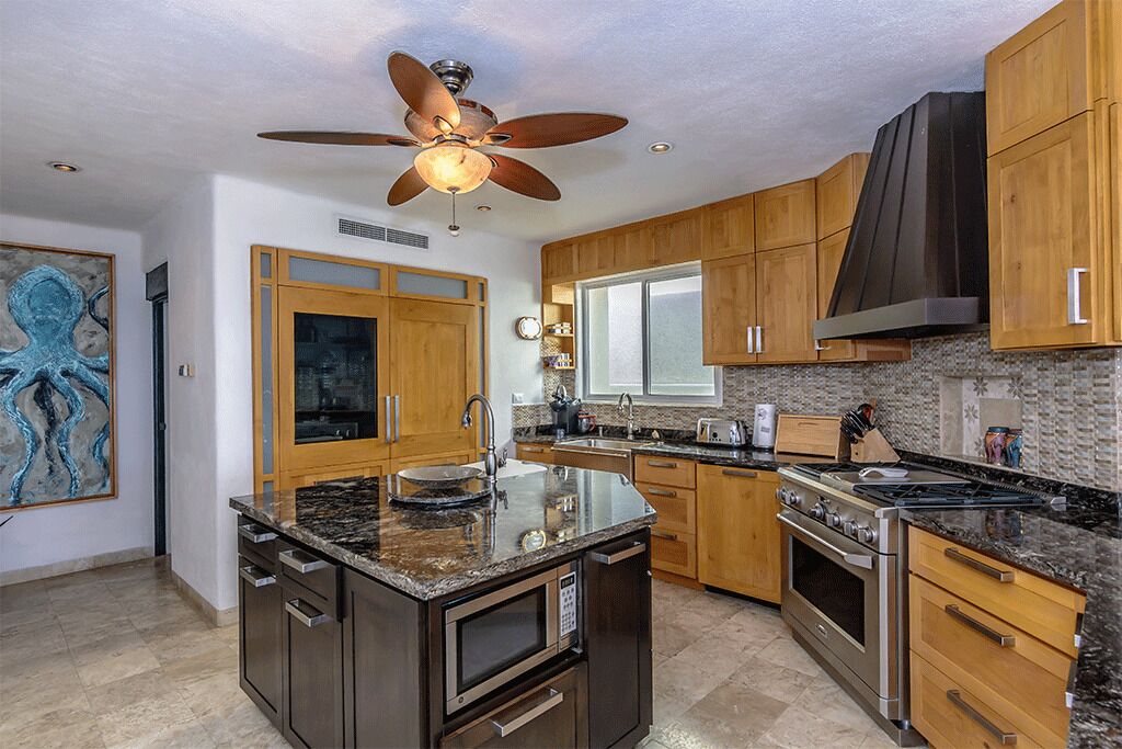 A modern kitchen with wooden cabinets, a granite countertop, stainless steel appliances, and a ceiling fan.
