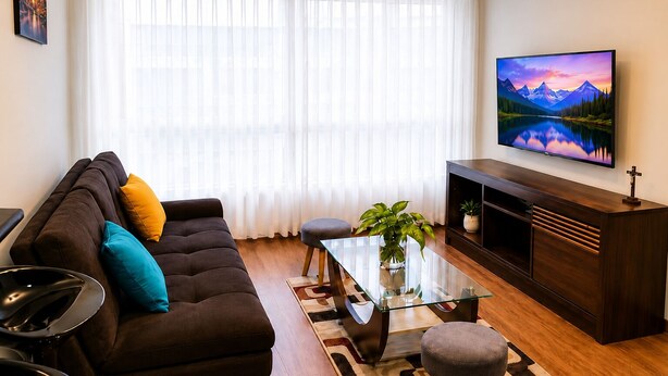 En stue med sofa, sofabord i glas, fjernsyn og en plante.