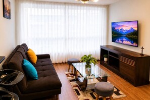 Ein Wohnzimmer mit einer Couch, einem Glastisch, einem Fernseher und einer Pflanze.