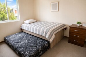 A bedroom with a bed, a bench, a dresser, and a window.