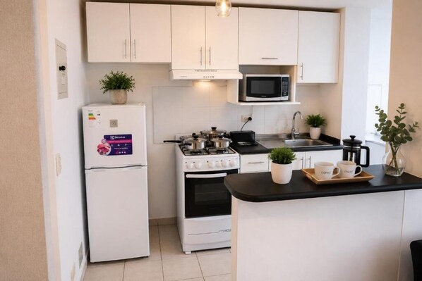 A compact kitchen with white cabinets, a microwave, a stove, and a refrigerator.