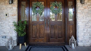 A wooden double door with two wreaths, a potted plant, and two lanterns on either side. - Longhorn Getaway in Dripping springs (Dripping Springs)