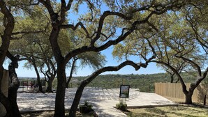 A paved outdoor area with white chairs arranged in rows, surrounded by trees and a wooden fence. - Longhorn Getaway in Dripping springs (Dripping Springs)