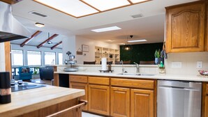 A modern kitchen with wooden cabinets, a stainless steel dishwasher, and a large window. - Longhorn Getaway in Dripping springs (Dripping Springs)