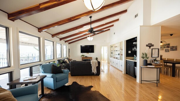A spacious living area with a large wooden ceiling, a black sofa, a blue armchair, and a cowhide rug. - Longhorn Getaway in Dripping springs (Dripping Springs)