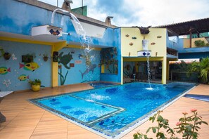 Uma piscina com cascata, rodeada por um mural colorido com peixes e criaturas marinhas.