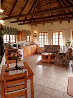Un espacio habitable amplio con una mesa de comedor de madera, un sofá estampado y una cocina con armarios de madera y techo de paja.