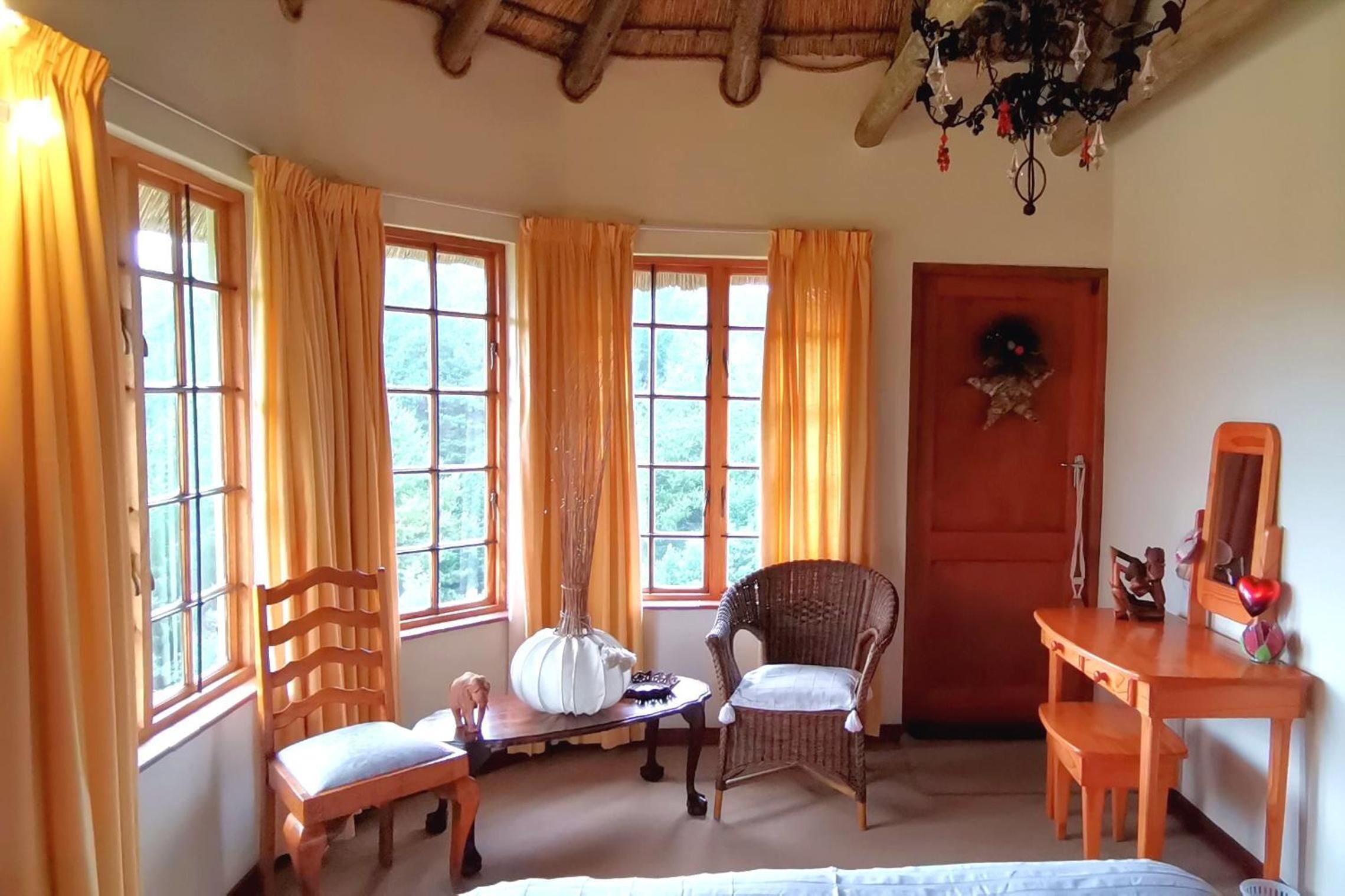 A room with large windows, a wooden desk, two chairs, a bed, and a chandelier.