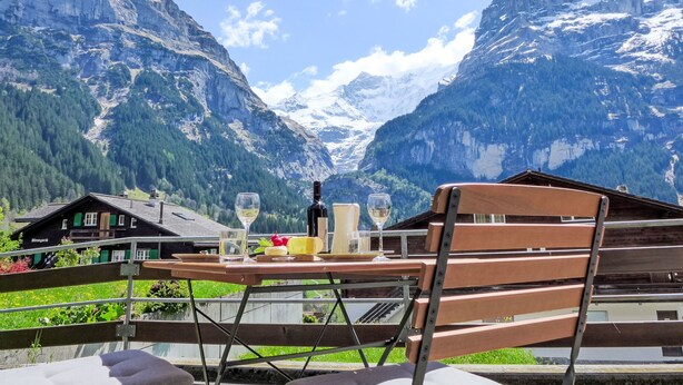 A table with a bottle and glasses, set against a mountain backdrop. - Chalet Almis-Bödeli by Interhome (Grindelwald)