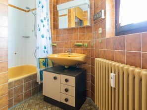 Un baño con un lavamanos amarillo, una bañera, un espejo y un radiador.