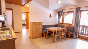 A kitchen with a wooden table and chairs, a built-in cabinet, and a window with curtains. - Voithofer by Interhome (Königsleiten)
