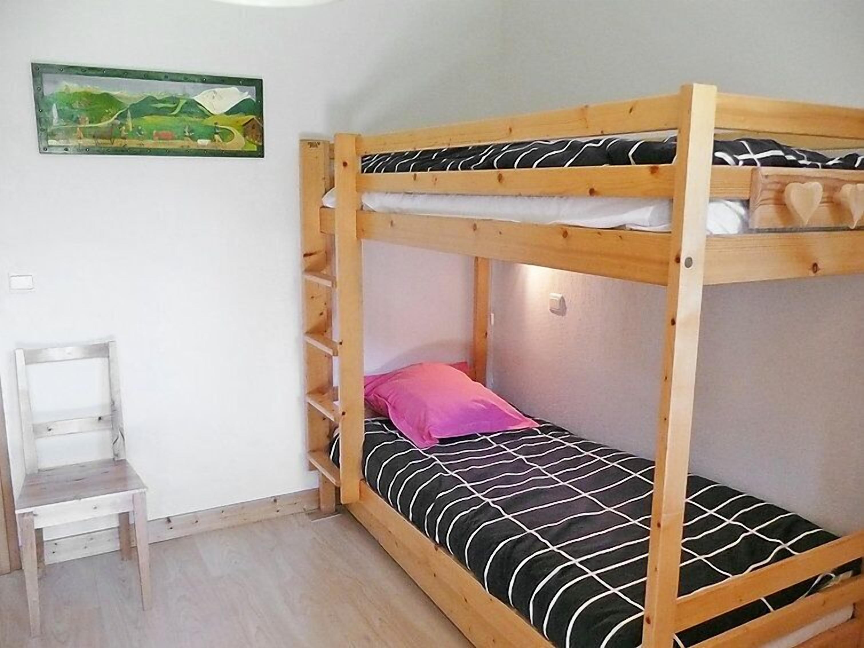 Un lit superposé avec une couvre-lit à rayures noires et blanches, un oreiller rose et une petite chaise en bois.