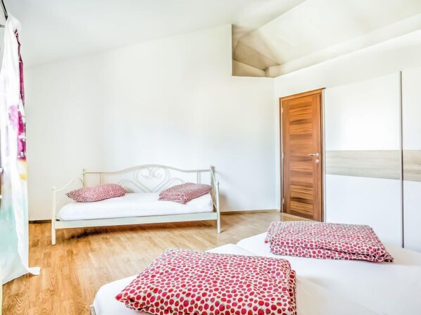 Een slaapkamer met een wit metalen bed, twee kussens, een houten deur en een witte muur.