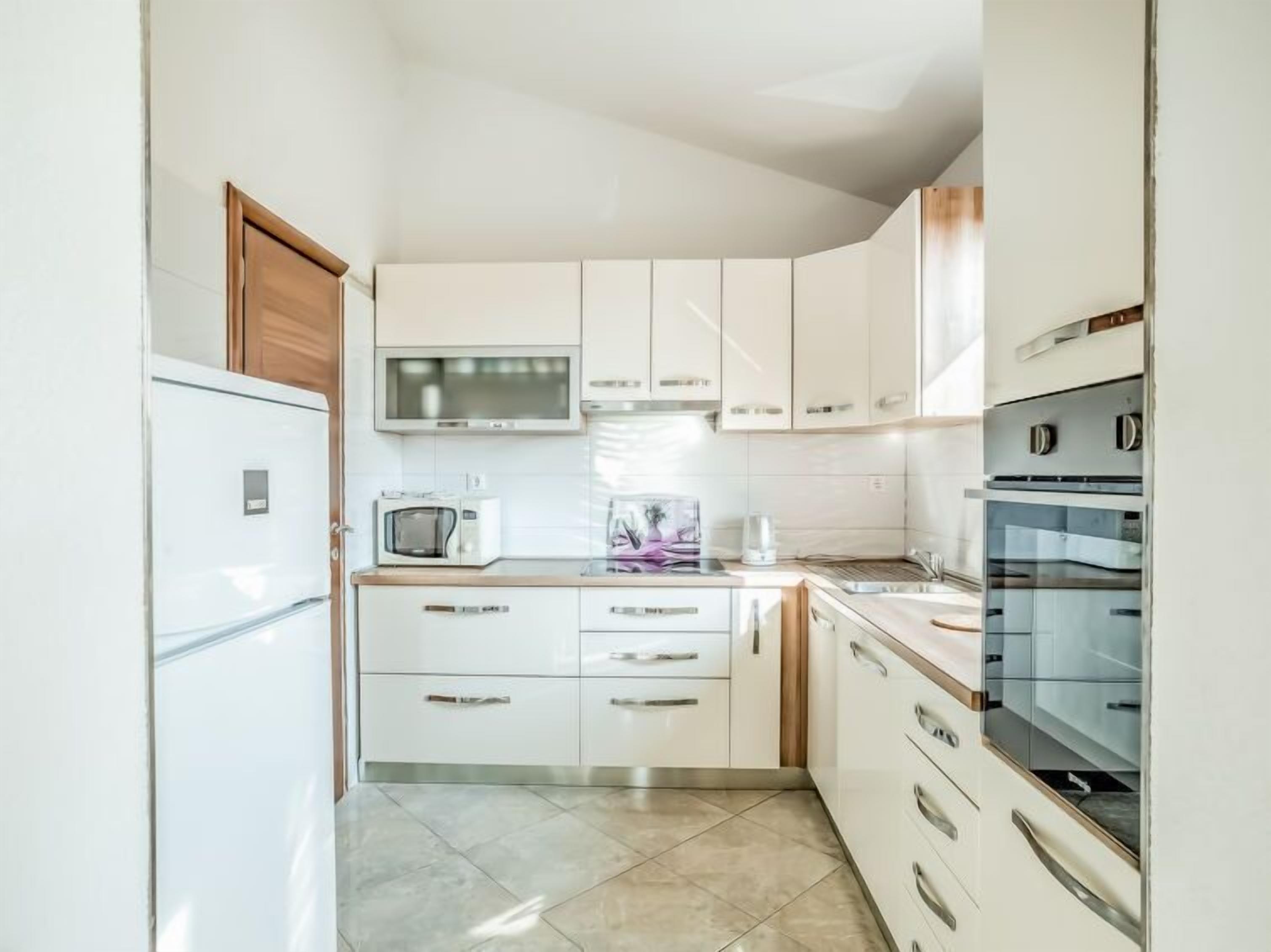 A compact kitchen with white cabinets, a microwave, a coffee maker, and a built-in oven.