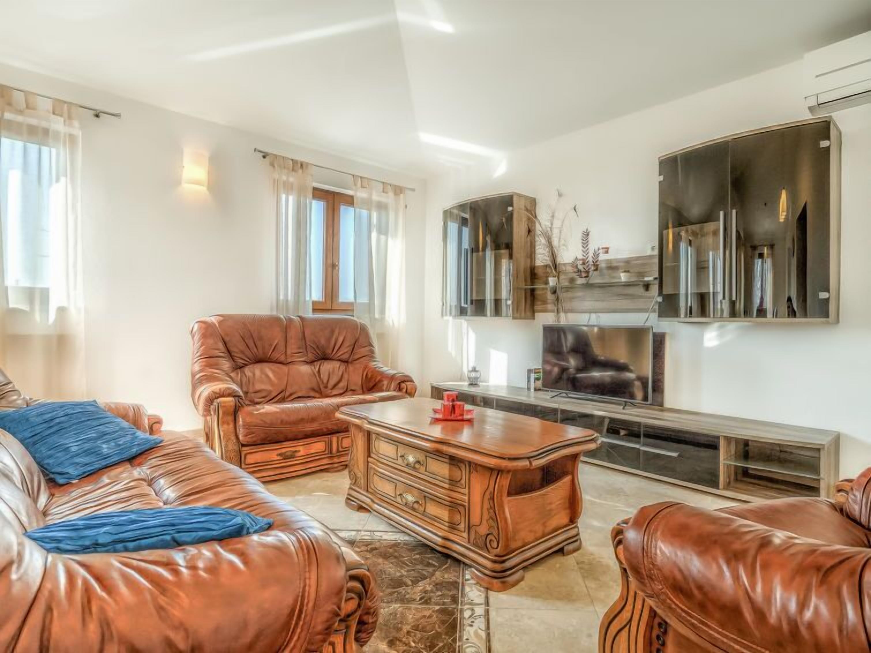A spacious living room with leather sofas, a wooden coffee table, and a large flat-screen TV mounted on the wall.