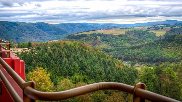 Vista panorámica desde un balcón sobre un valle con bosques densos y colinas ondulantes.