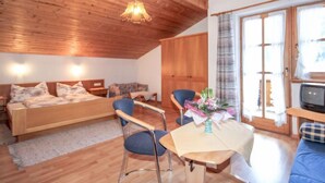 Ein gemütliches Zimmer mit Holzbalkendecke, einem Bett, einem Sofa, einem Tisch mit Blumen und einem Fernseher.