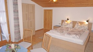 Ein Schlafzimmer mit einem hölzernen Bett, zwei Nachttischen, einem Holzstuhl, einem kleinen Tisch mit Kerze und einem Fenster mit Vorhängen.