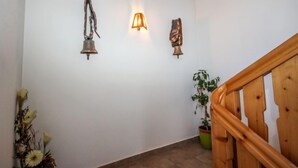 Ein Flur mit Holzboden, einer Holztreppe und einer Wand mit drei daran befestigten Gegenständen: einer Glocke, einer Lampe und einem dekorativen Objekt.