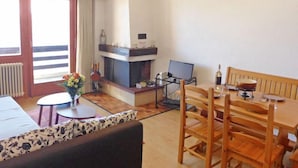 Una sala de estar con chimenea, una mesa de comedor con sillas, un sofá y una mesita auxiliar con un florero.