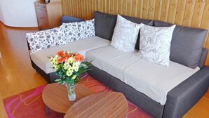 Una sala de estar moderna con un sofá gris, cojines estampados, una mesa de centro de madera y un jarrón de flores.