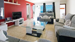 Ein modernes Wohnzimmer mit roter Akzentwand, einem Flachbildfernseher, einem Glastisch und zwei grauen Sofas.