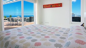 Ein Schlafzimmer mit Bett, Meerblick, einer Essecke mit Stühlen und Tisch sowie einem Bild an der Wand.